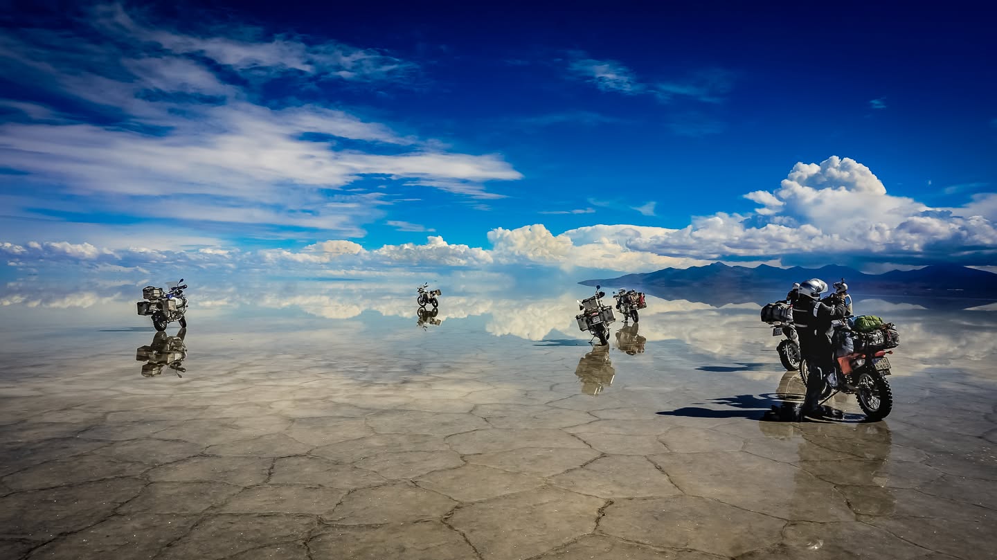 Motocykle stoją na lustrzanej tafli solniska Salar de Uyuni, niebo odbija się pod kołami.