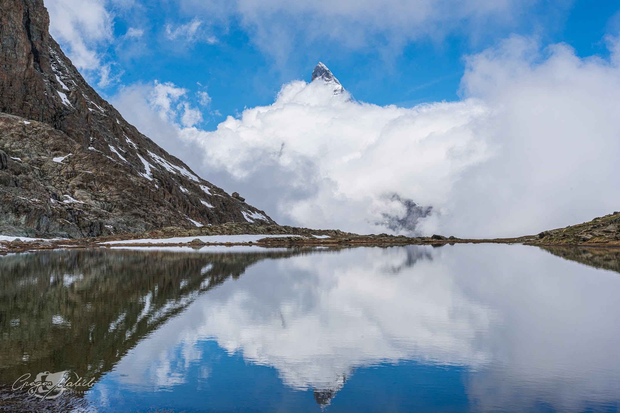 Matterhorn wynurza się z chmur i odbija w tafli jeziora Riffelsee.